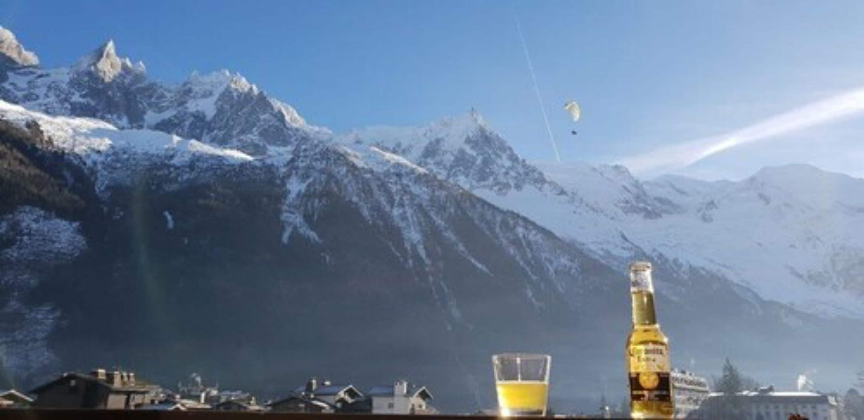 A mountain landscape with snow-covered peaks, a clear sky, and a bottle of beer on a table.