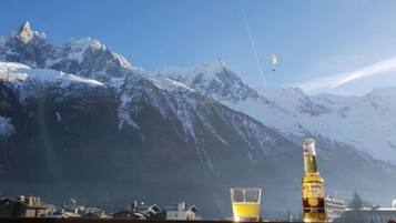 A mountain landscape with snow-covered peaks, a clear sky, and a bottle of beer on a table.