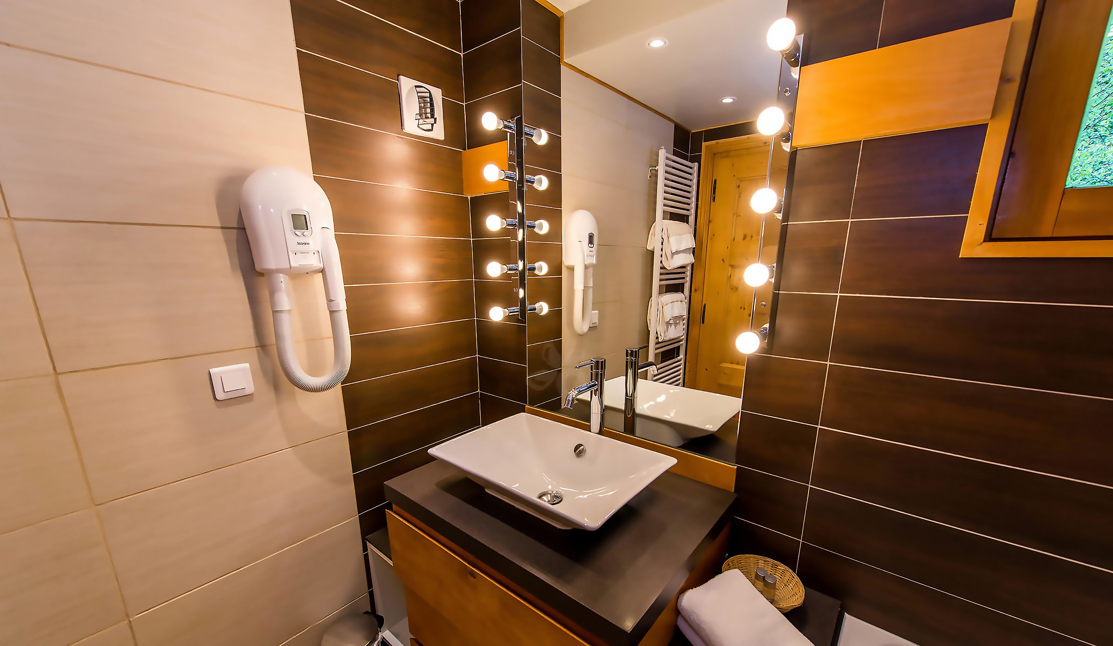 A modern bathroom with a large mirror, vanity, and a hairdryer on the wall.