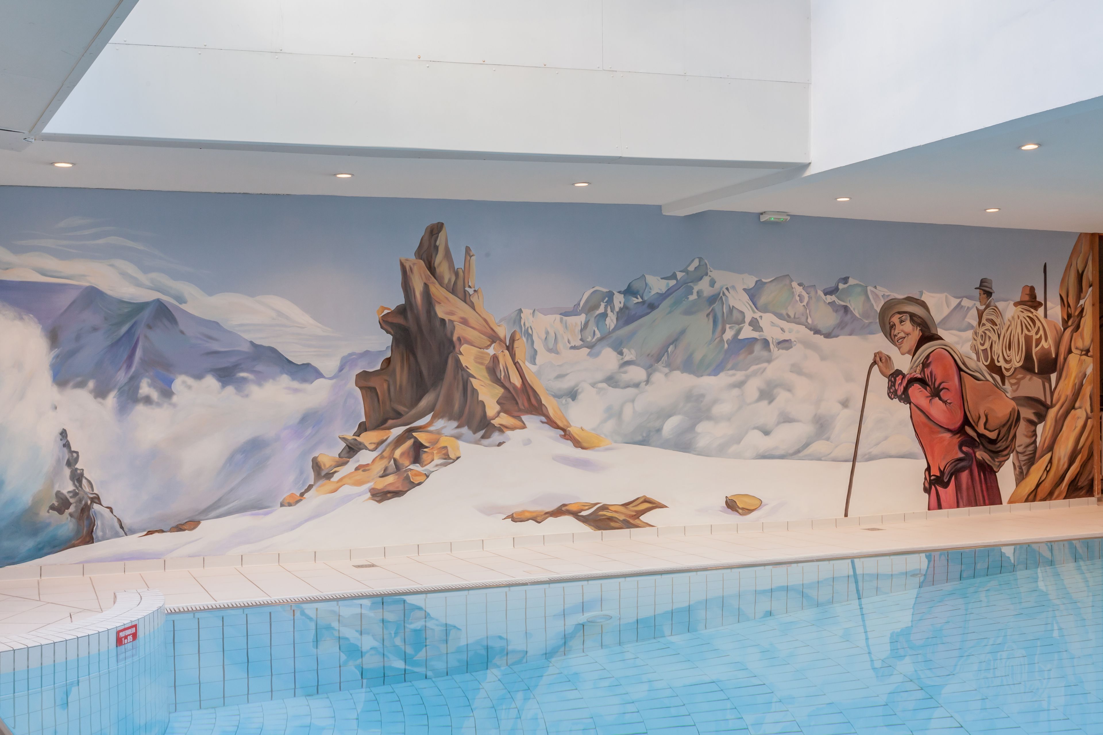 Una piscina con un mural de montañas y una persona con un bastón.