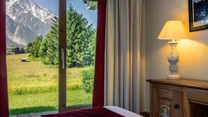 Quarto de hotel com cama, luminária, vista para uma montanha e porta para uma varanda.