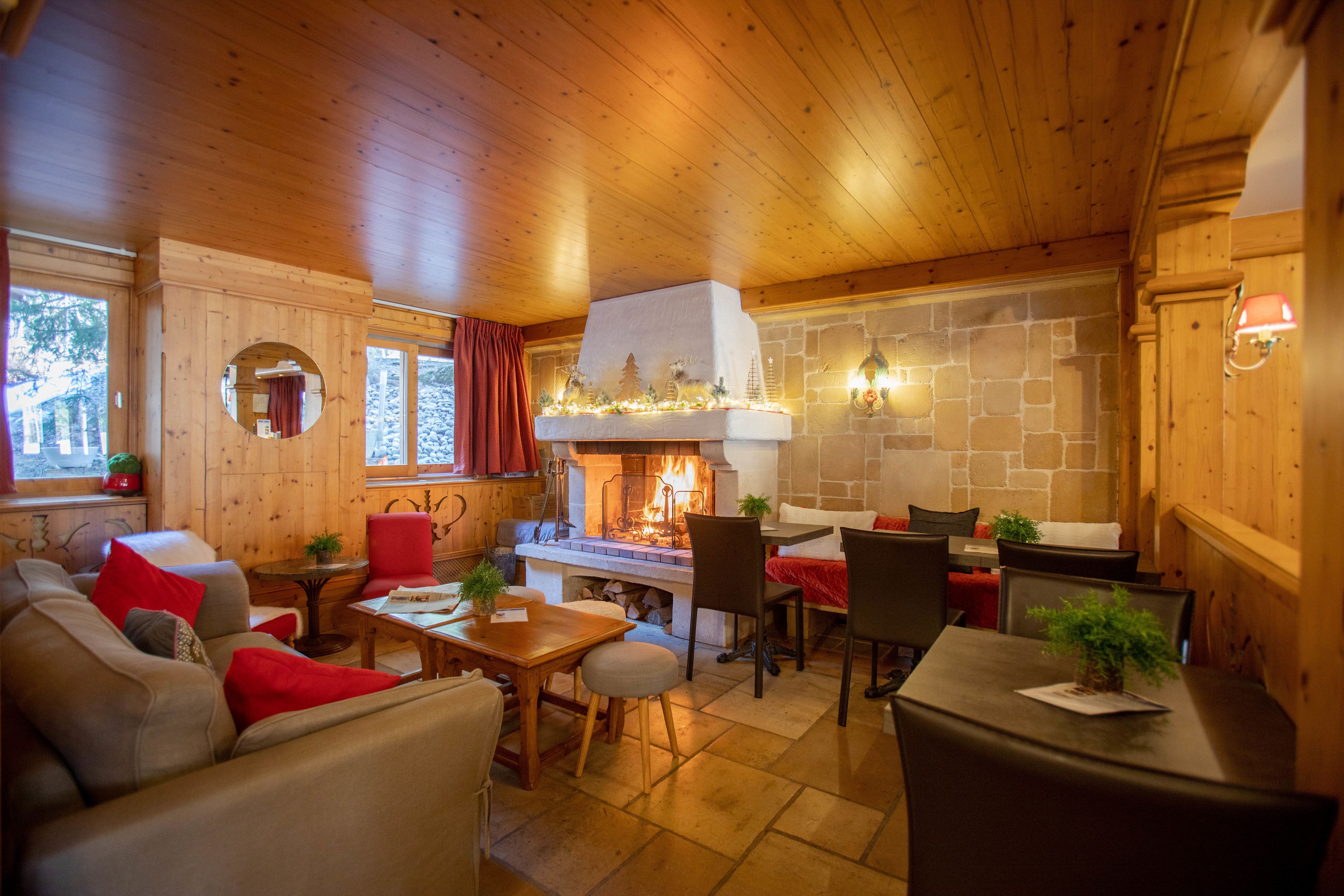 A cozy interior with wooden walls, a stone fireplace, and a dining area with chairs and tables.