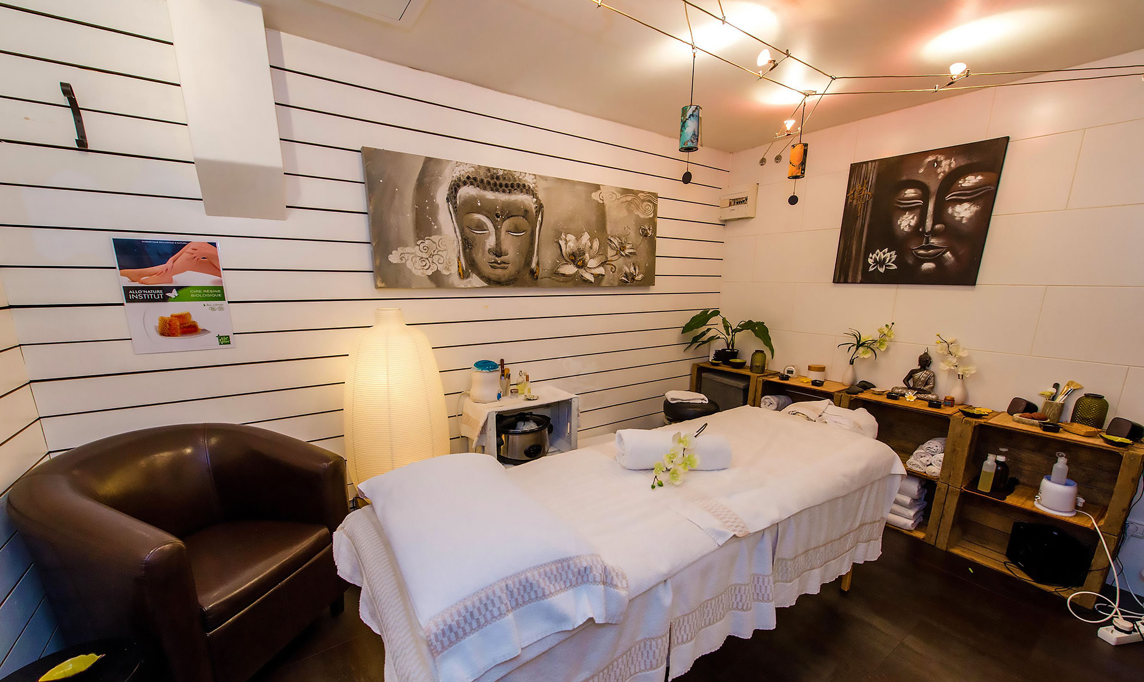 A spa room with a massage table, a massage chair, a shelf with spa products, and two wall-mounted paintings.