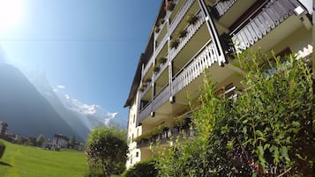 Un edificio de varios pisos con balcones, rodeado de vegetación y montañas al fondo.