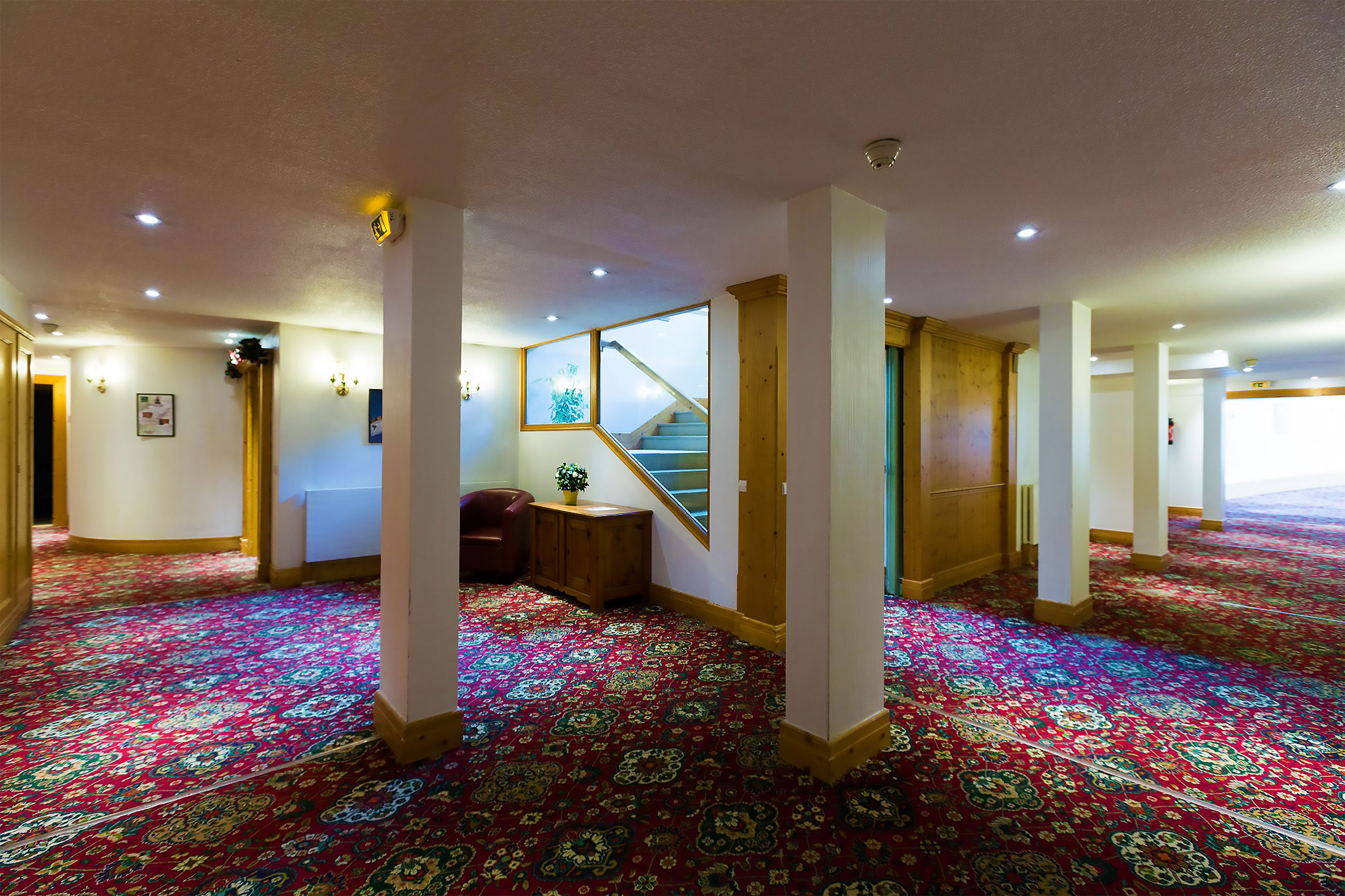 Un amplio vestíbulo de hotel con alfombra estampada, una escalera y un banco de madera.