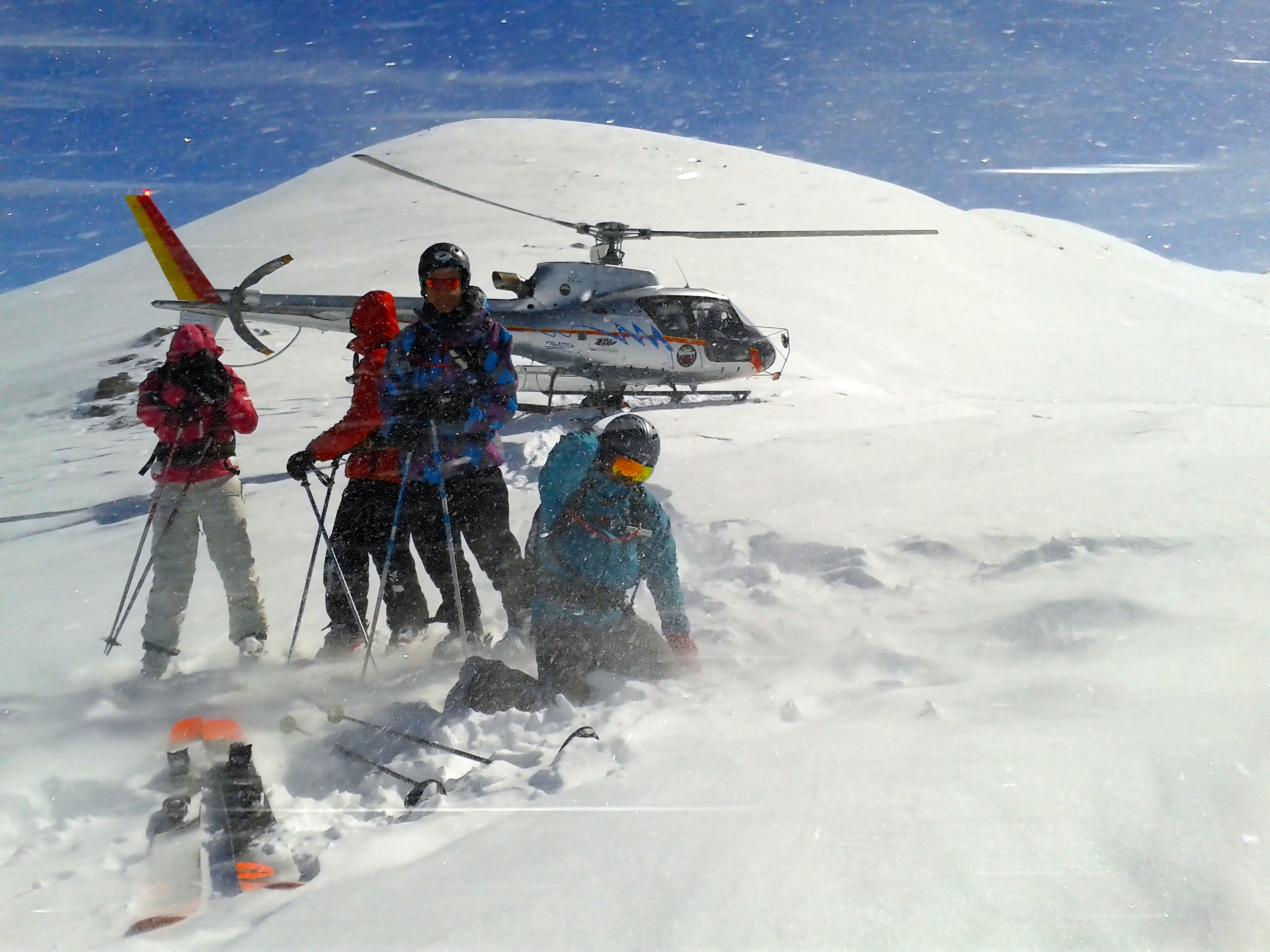 Un groupe de personnes se trouve sur une montagne enneigée, avec un hélicoptère en arrière-plan.