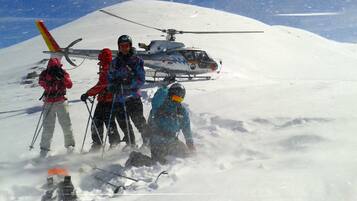 Un groupe de personnes se trouve sur une montagne enneigée, avec un hélicoptère en arrière-plan.