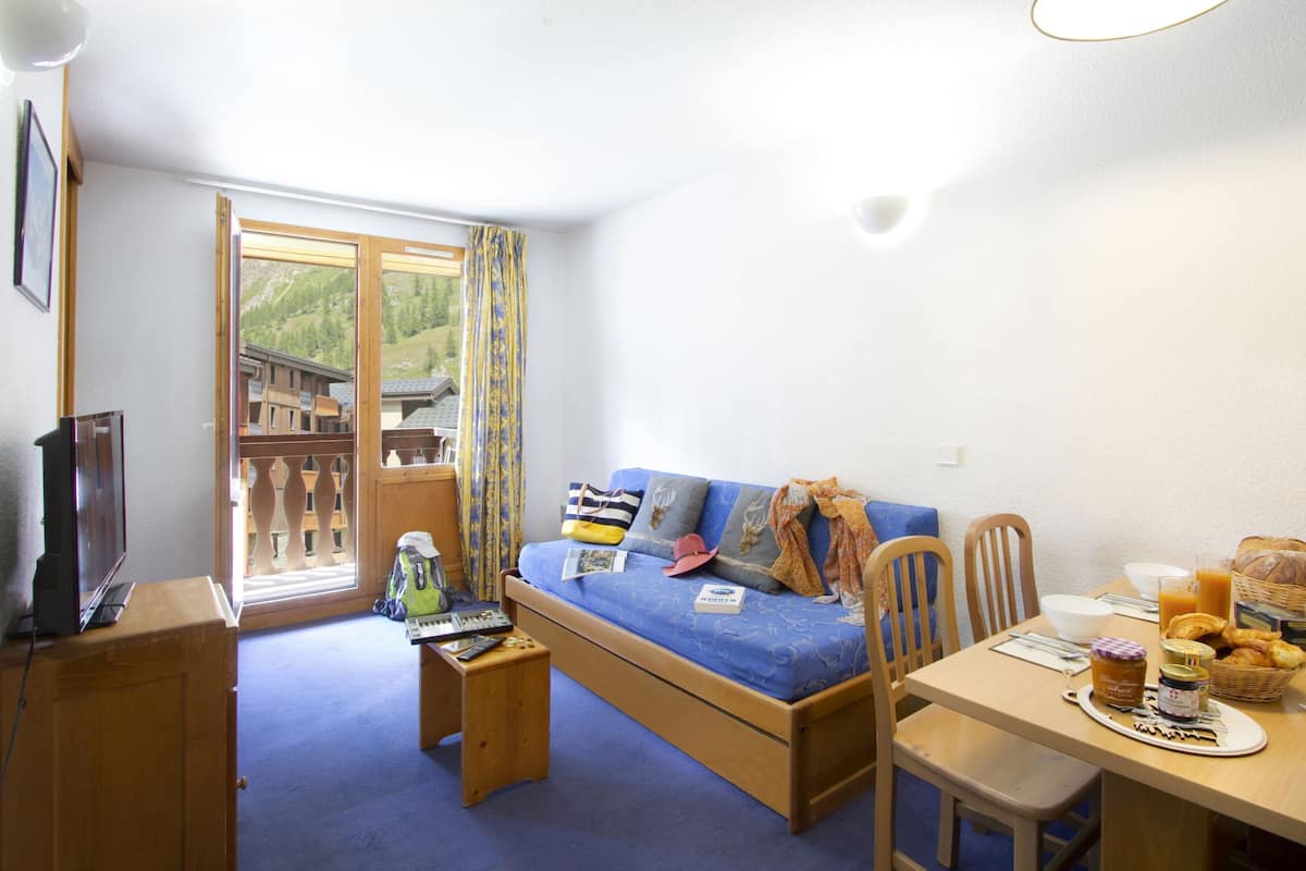 Une chambre de taille modeste comprenant un lit, une table à manger avec des articles pour le petit-déjeuner, un téléviseur et une vue sur une montagne par la fenêtre.