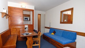 Een knus kamertje met een houten bankje, een tafeltje, een blauwe bank en een spiegel aan de muur.