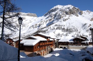 A snow-covered mountain resort with wooden buildings and a clear blue sky. - Résidence Odalys Les Jardins de Val - Les Verdets (Val-d'Isere)