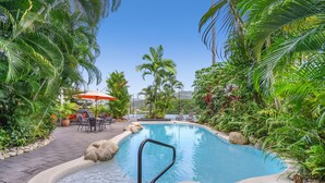 Piscina rodeada de plantas tropicales y un patio con mobiliario de exterior.