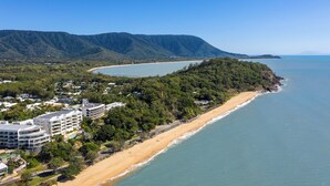 Un hotel costero con varios pisos, vista a la playa y montañas al fondo.
