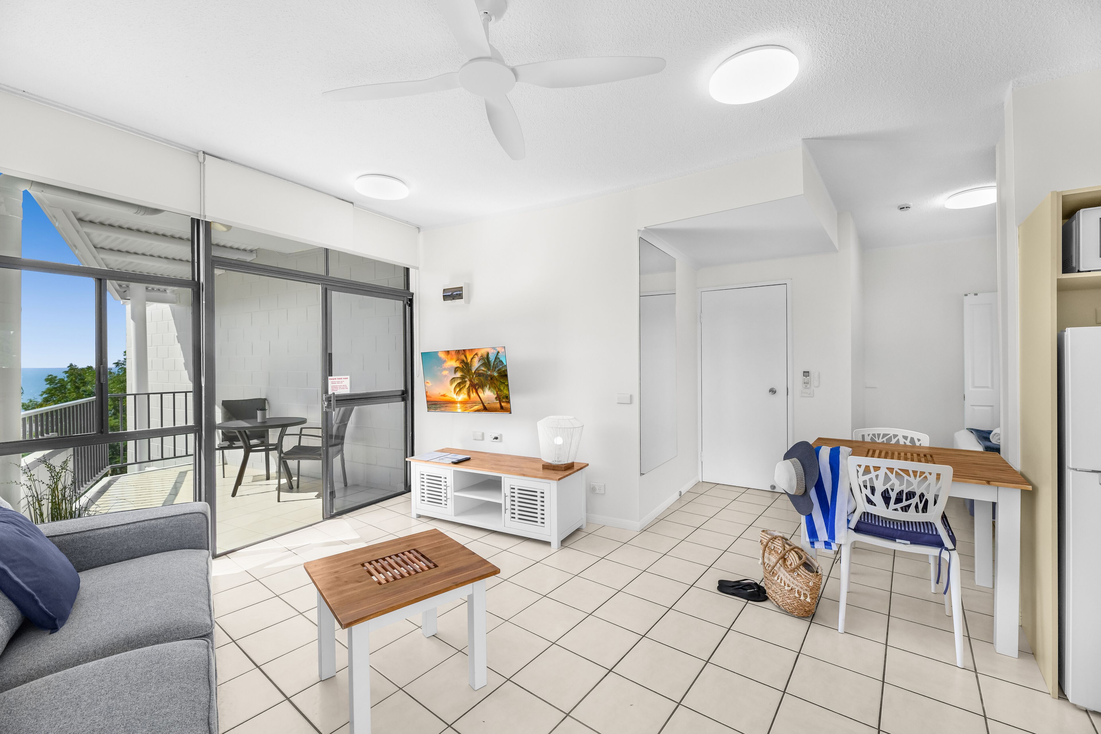 A modern living room with a sofa, a wooden table, a TV, and a balcony with a view.