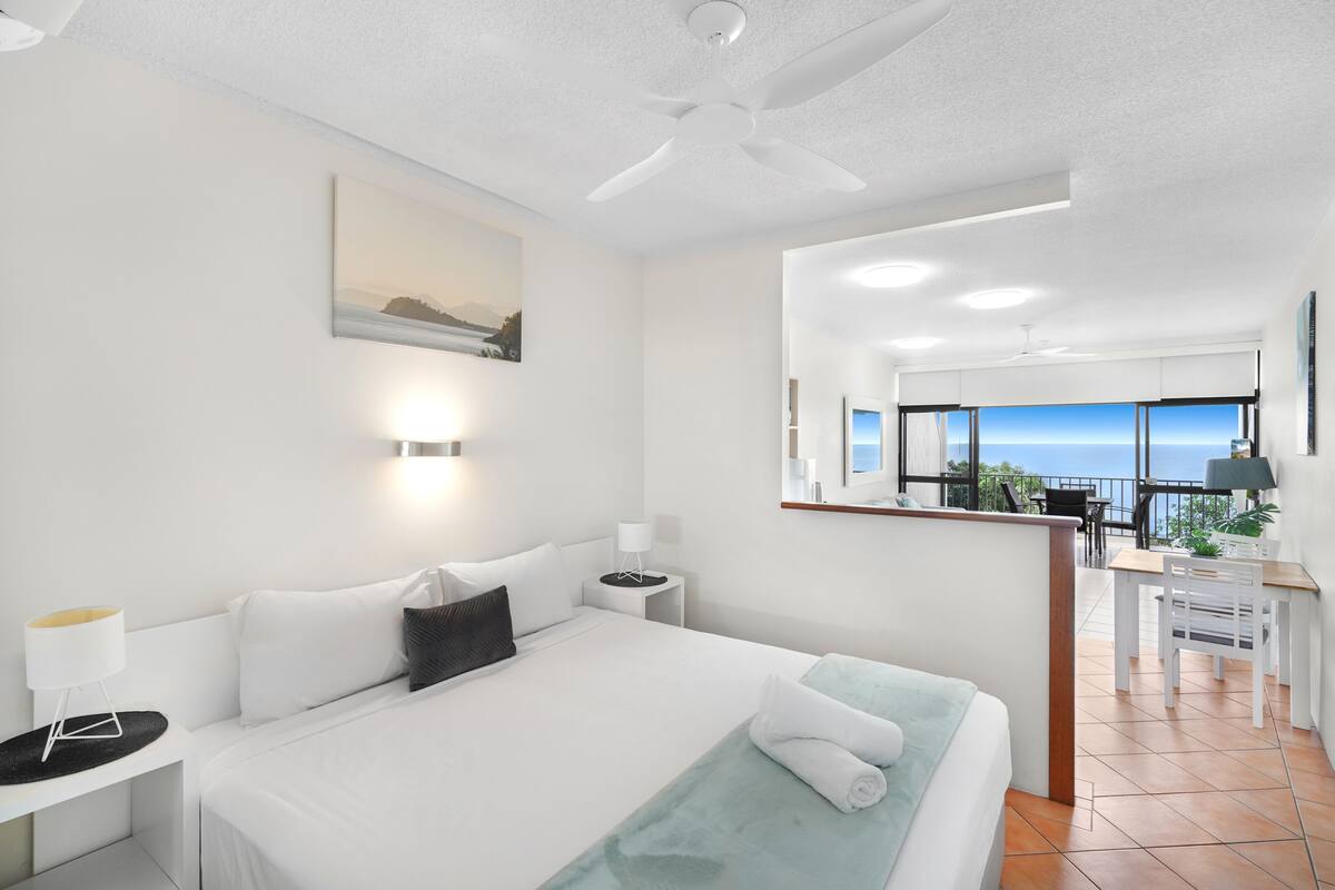 A modern hotel room with a large bed, a desk, and a balcony with a view.