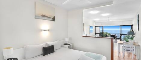 A modern hotel room with a large bed, a desk, and a balcony with a view.
