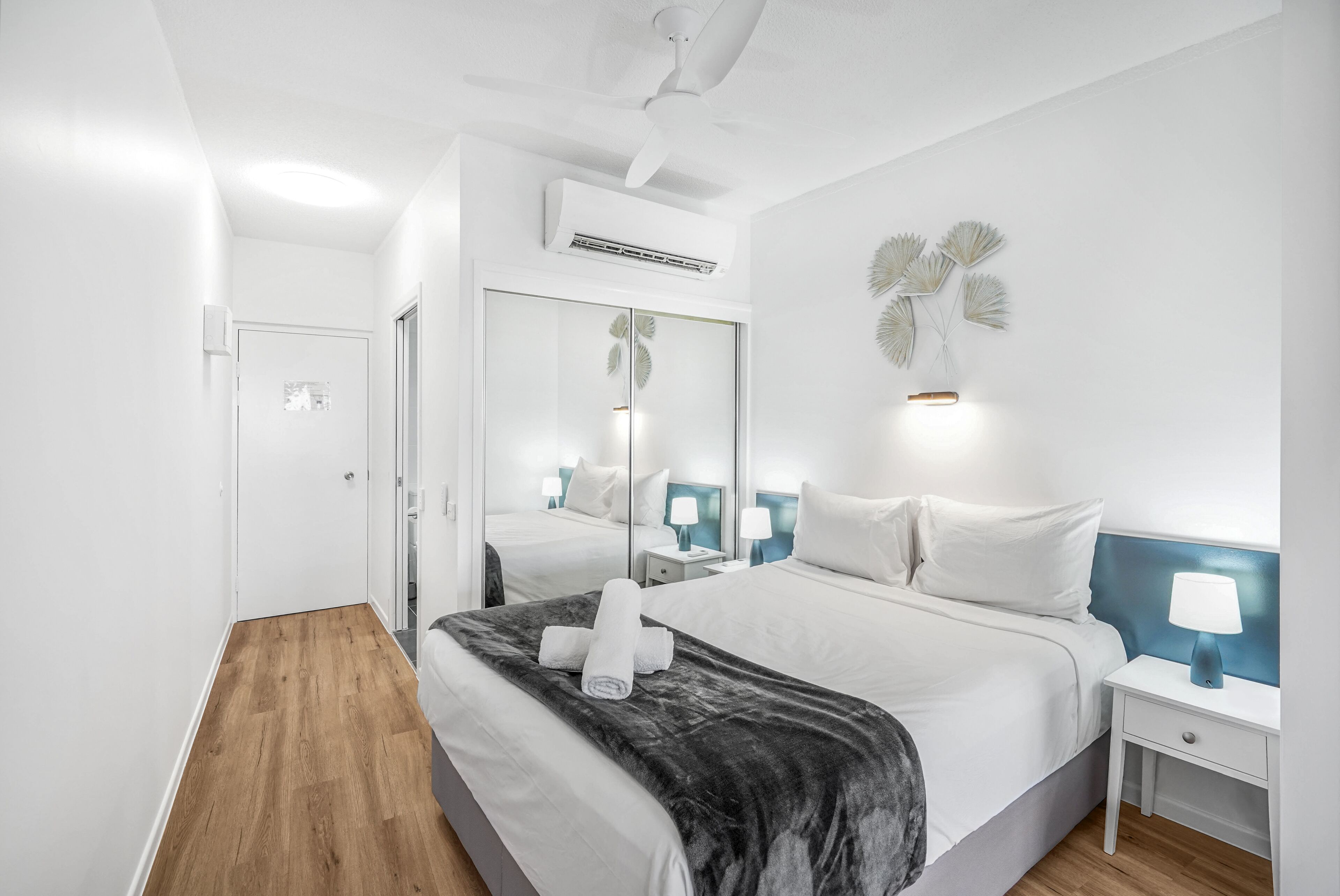 A modern hotel room with a large bed, bedside tables, a ceiling fan, and a wall-mounted air conditioner.