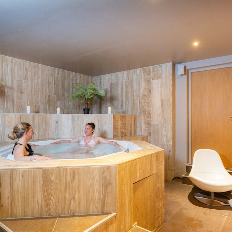 A spa room with a hot tub, wooden walls, and two potted plants.