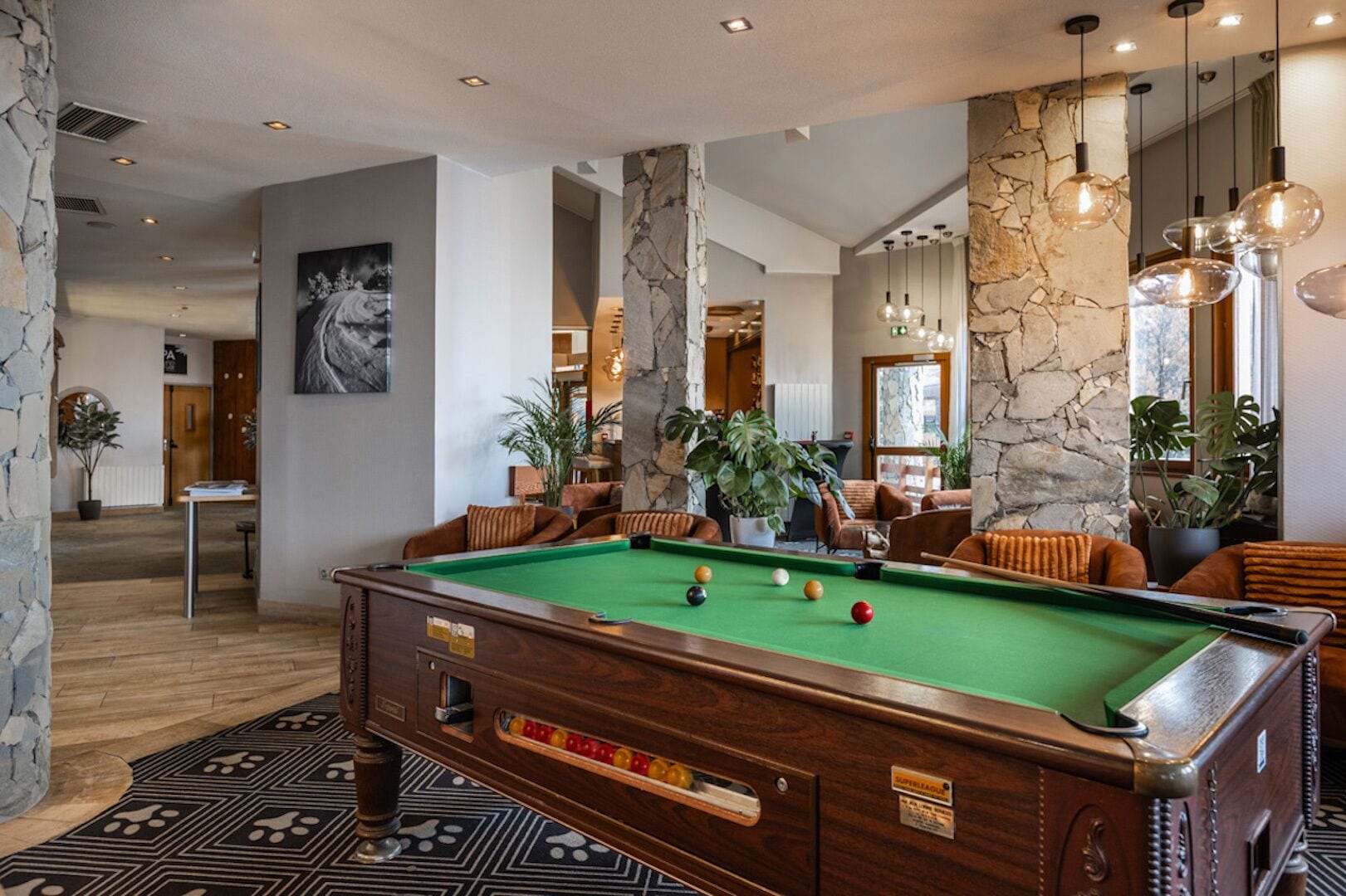 A pool table in a modern room with stone walls, wooden flooring, and comfortable seating.