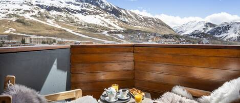 A wooden deck with a table set for breakfast, overlooking snow-capped mountains.