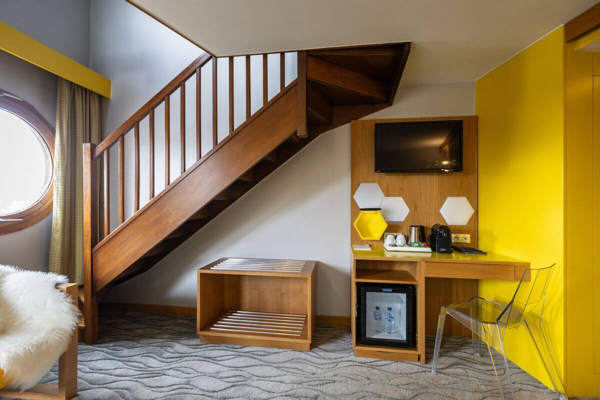 Ein modernes Hotelzimmer mit einer Holztreppe, einem Schreibtisch mit Computer, einem Flachbildfernseher und einem kleinen Kühlschrank.