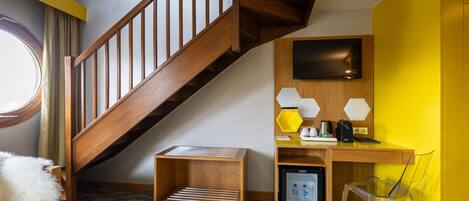 Una habitación de hotel moderna con una escalera de madera, un escritorio con computadora, un televisor de pantalla plana y un refrigerador pequeño.