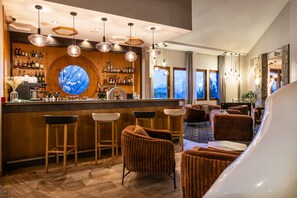 A bar area with wooden bar stools, a round mirror, and a variety of bottles. There are cushioned seating areas with a view of the outdoors.