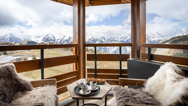 A wooden deck with a table set for tea and pastries, overlooking a mountainous landscape.