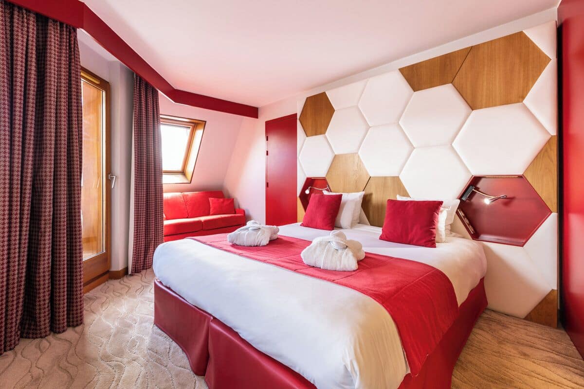 Ein Hotelzimmer mit einem großen Bett, rot-weißer Bettwäsche, einer sechseckigen Wandgestaltung und einer roten Akzentwand.