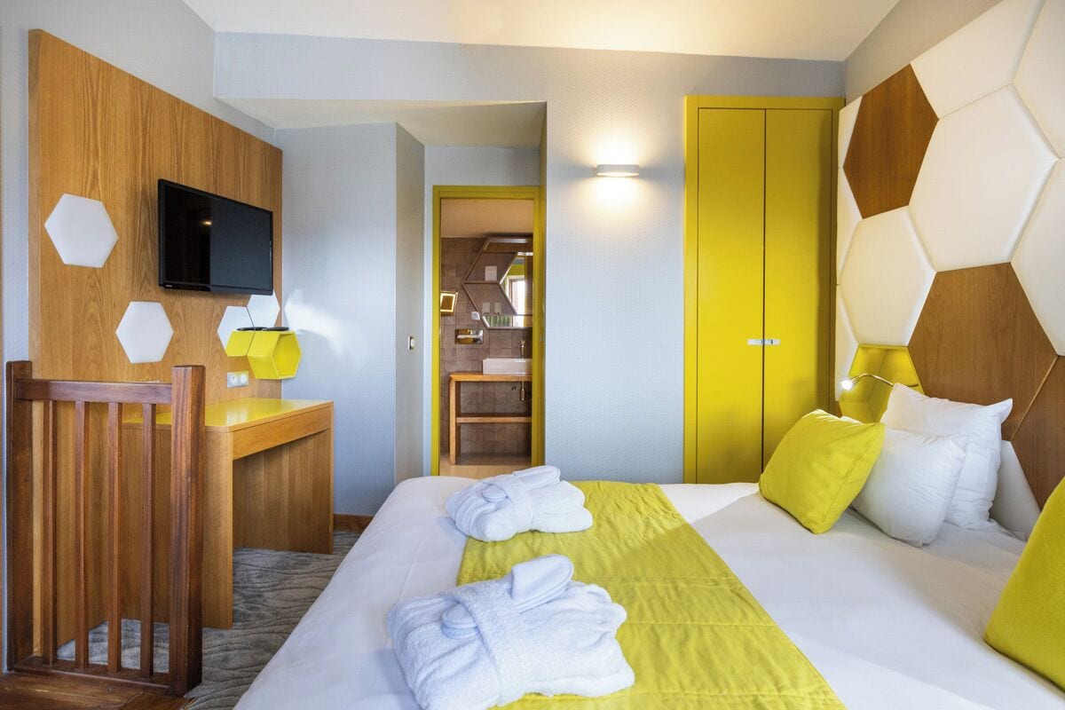 Habitación de hotel con cama, escritorio, televisión y baño visible a través de una puerta abierta.