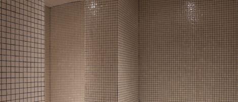 A bathroom with tiled walls and floor, a shower area, and a bench.