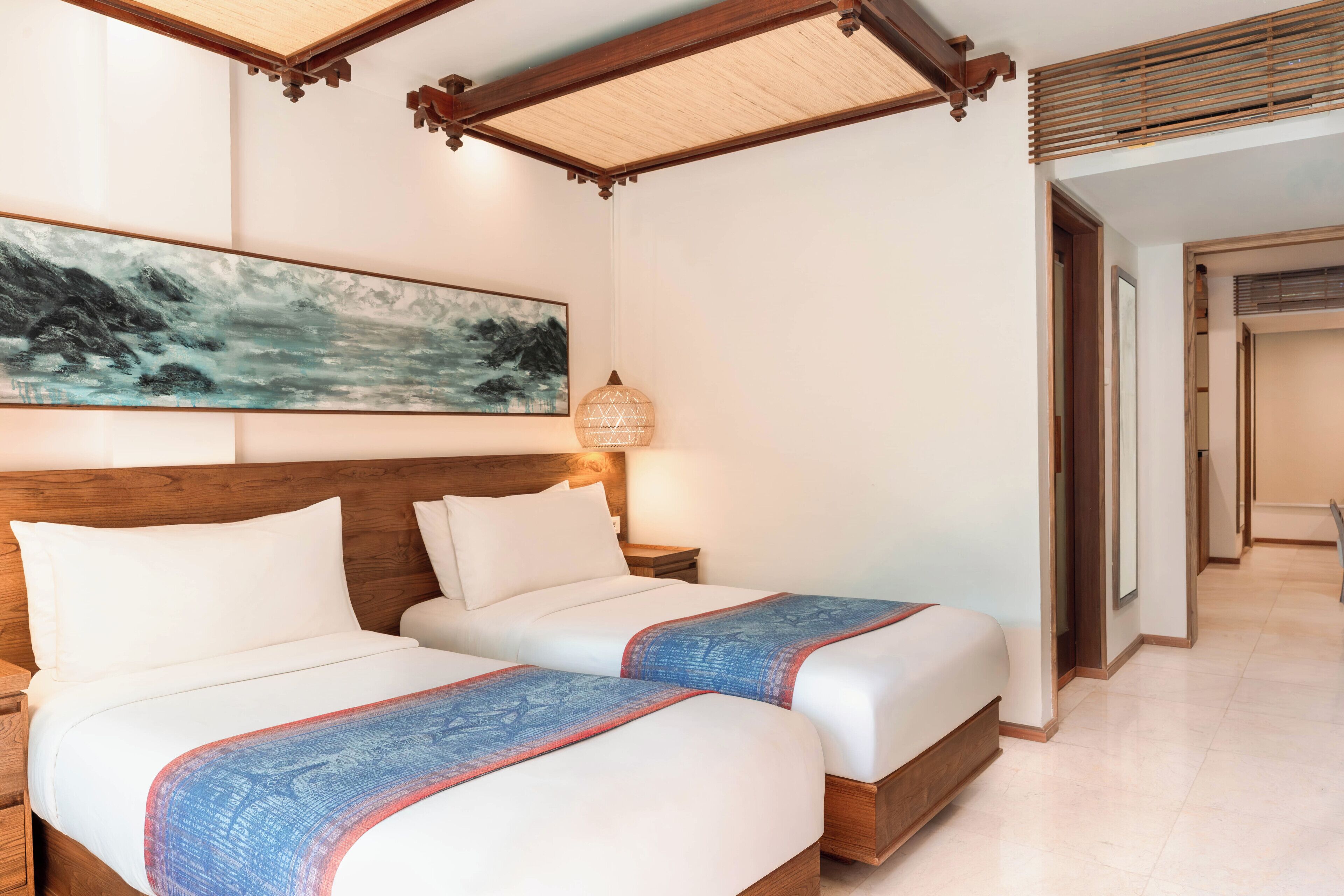 A hotel room with two beds, a wooden headboard, a wall painting, a hanging lamp, and a tiled floor.