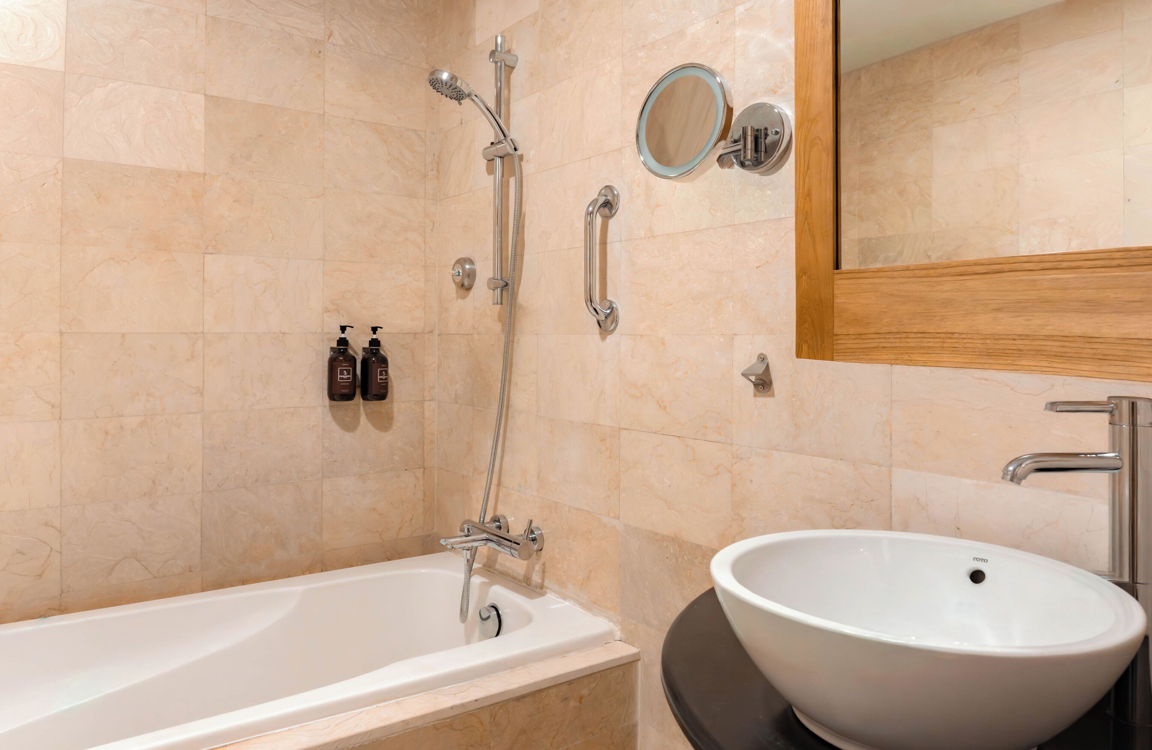 A bathroom with a bathtub, a sink, a showerhead, a handheld shower, a mirror, and two bottles of shampoo.
