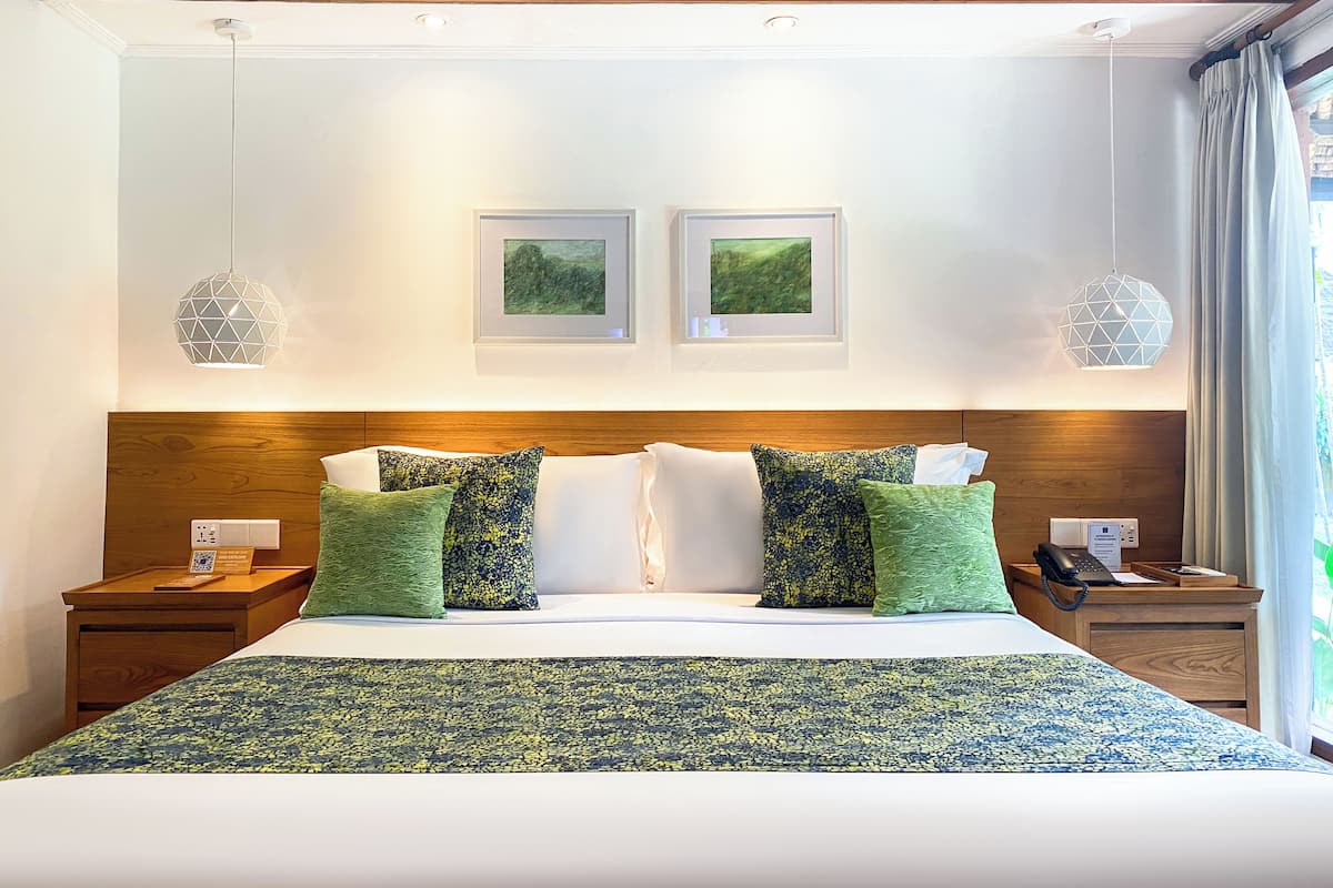 A hotel room with a large bed, two framed pictures on the wall, a wooden headboard, and a nightstand with a phone and a tray.