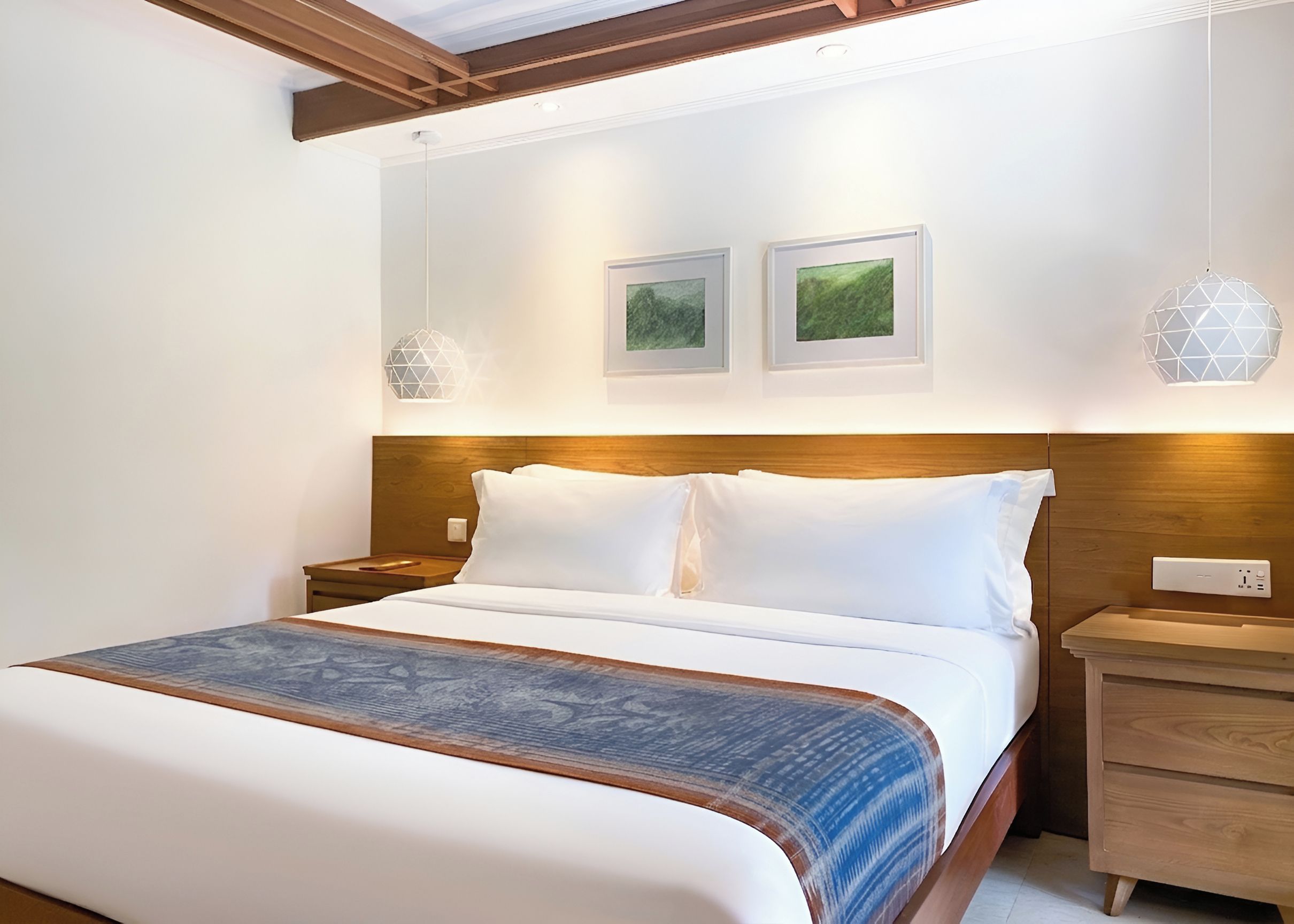 Une chambre d’hôtel avec un grand lit, deux tables de chevet, une tête de lit en bois et deux tableaux encadrés accrochés au mur.