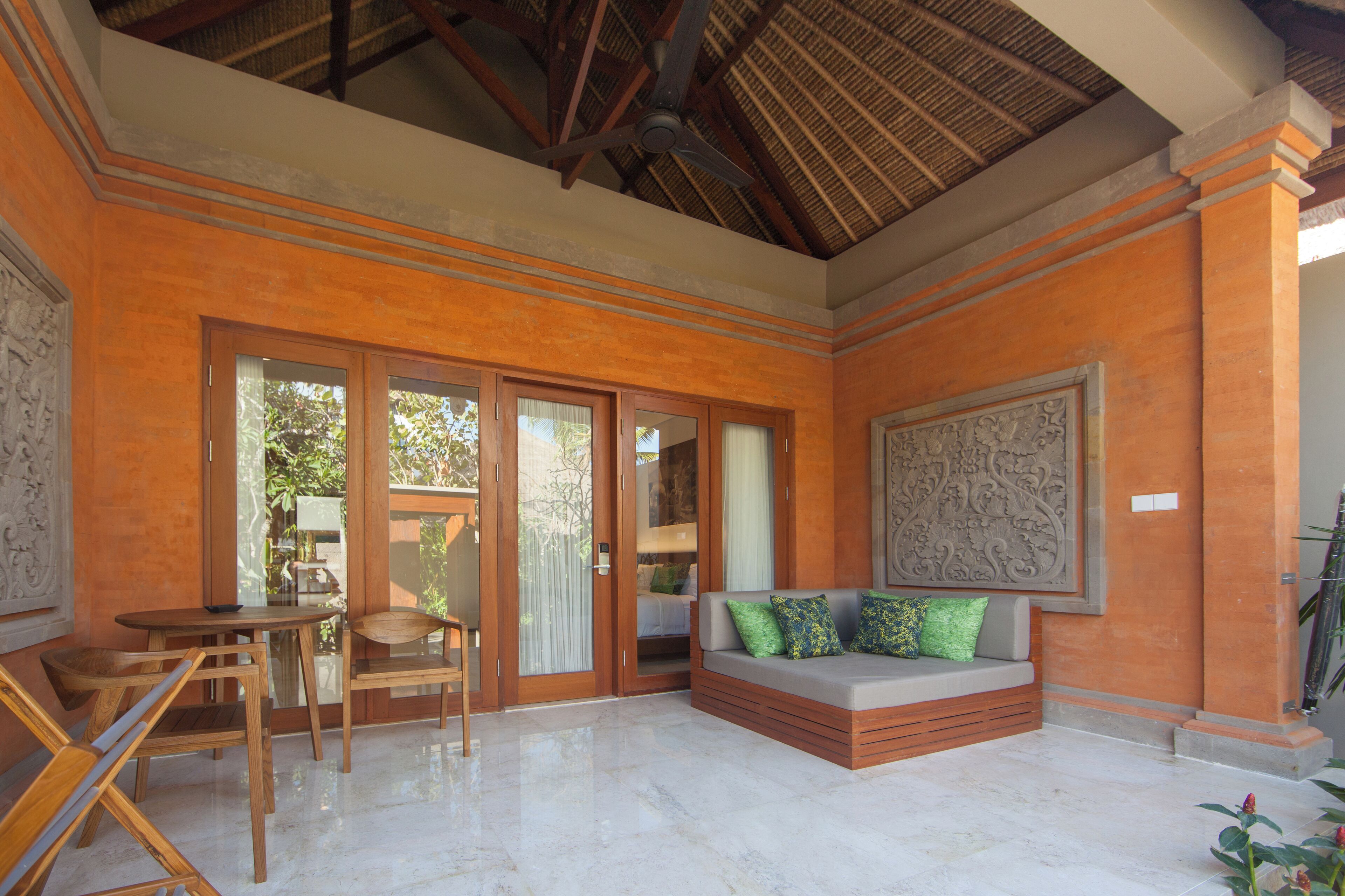 A room with a wooden bench, a table, and chairs. There is a large window and a door leading outside.