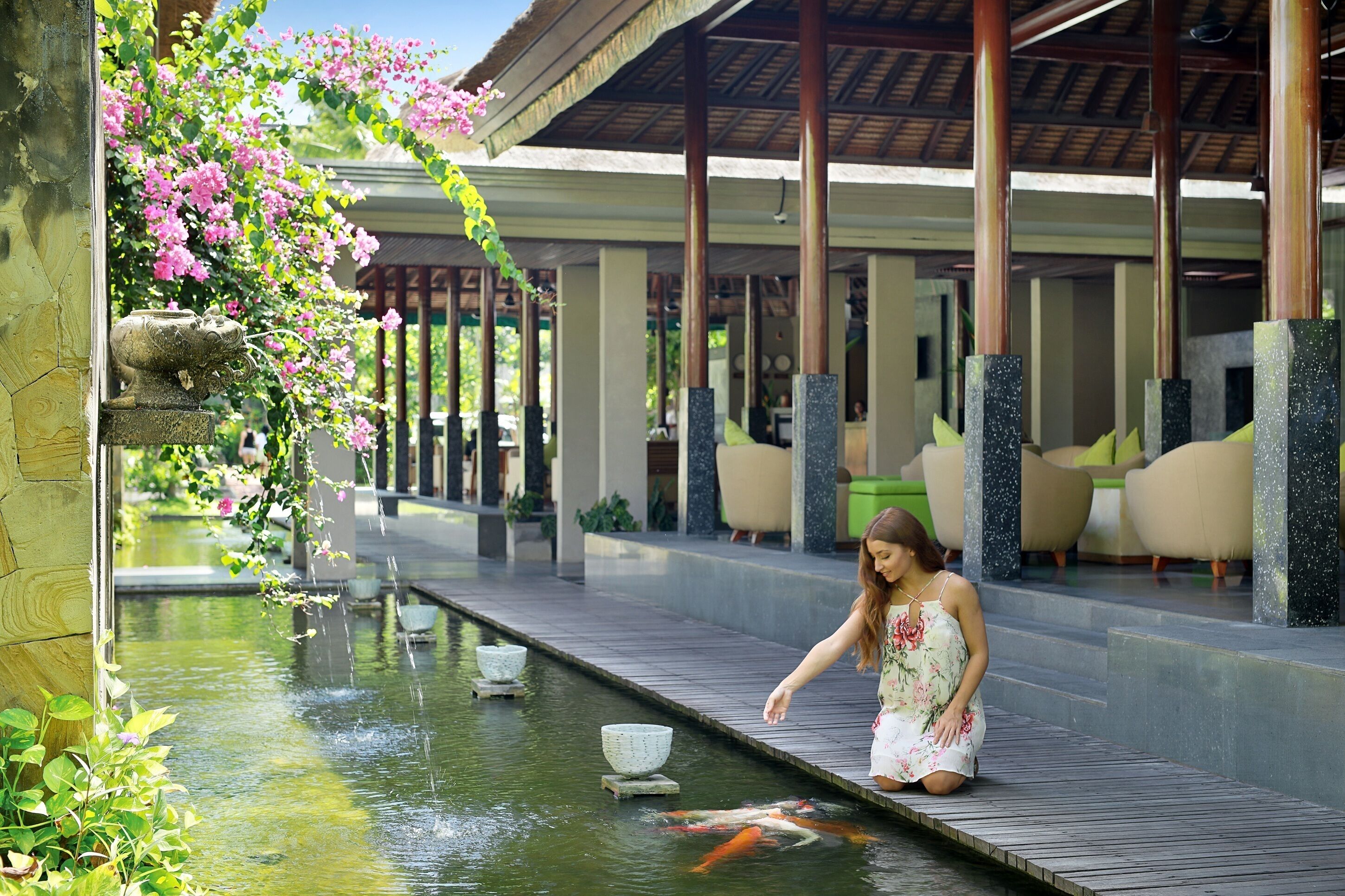 A koi pond with a stone basin, a wooden walkway, and a covered seating area with chairs.