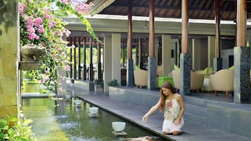 A koi pond with a stone basin, a wooden walkway, and a covered seating area with chairs.