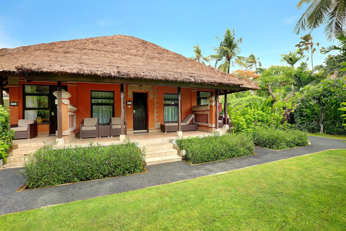 A house with a thatched roof, a porch with outdoor furniture, and a well-maintained garden.