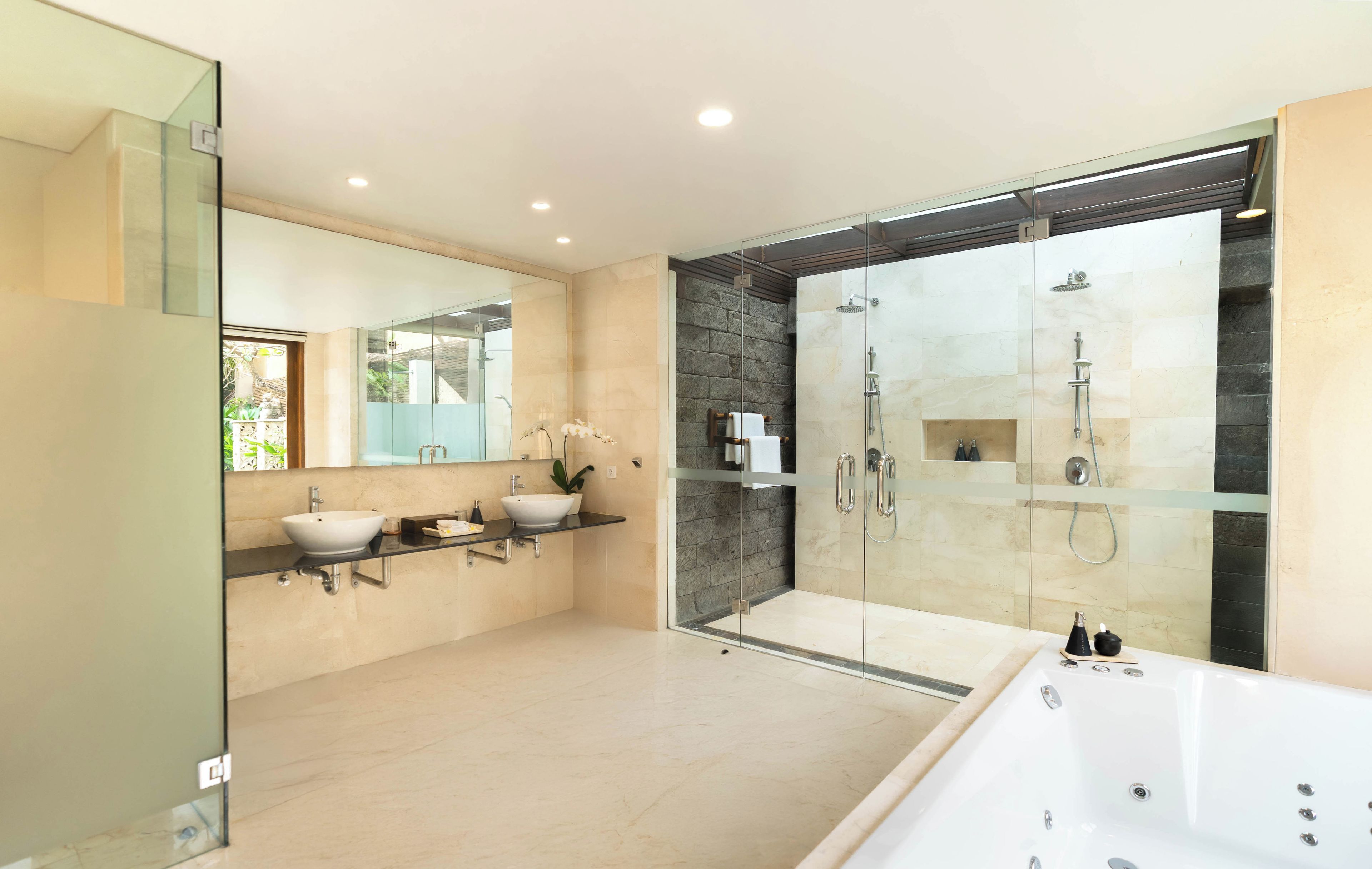 Un baño moderno con ducha de vidrio, dos lavamanos y una bañera grande.