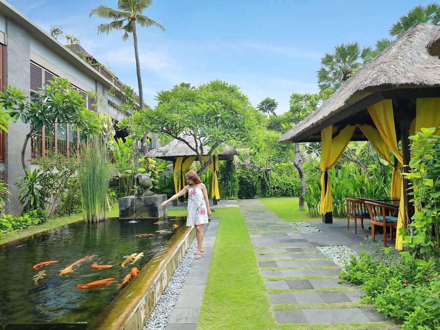 A serene garden with a koi pond, a pathway, and thatched-roof structures.
