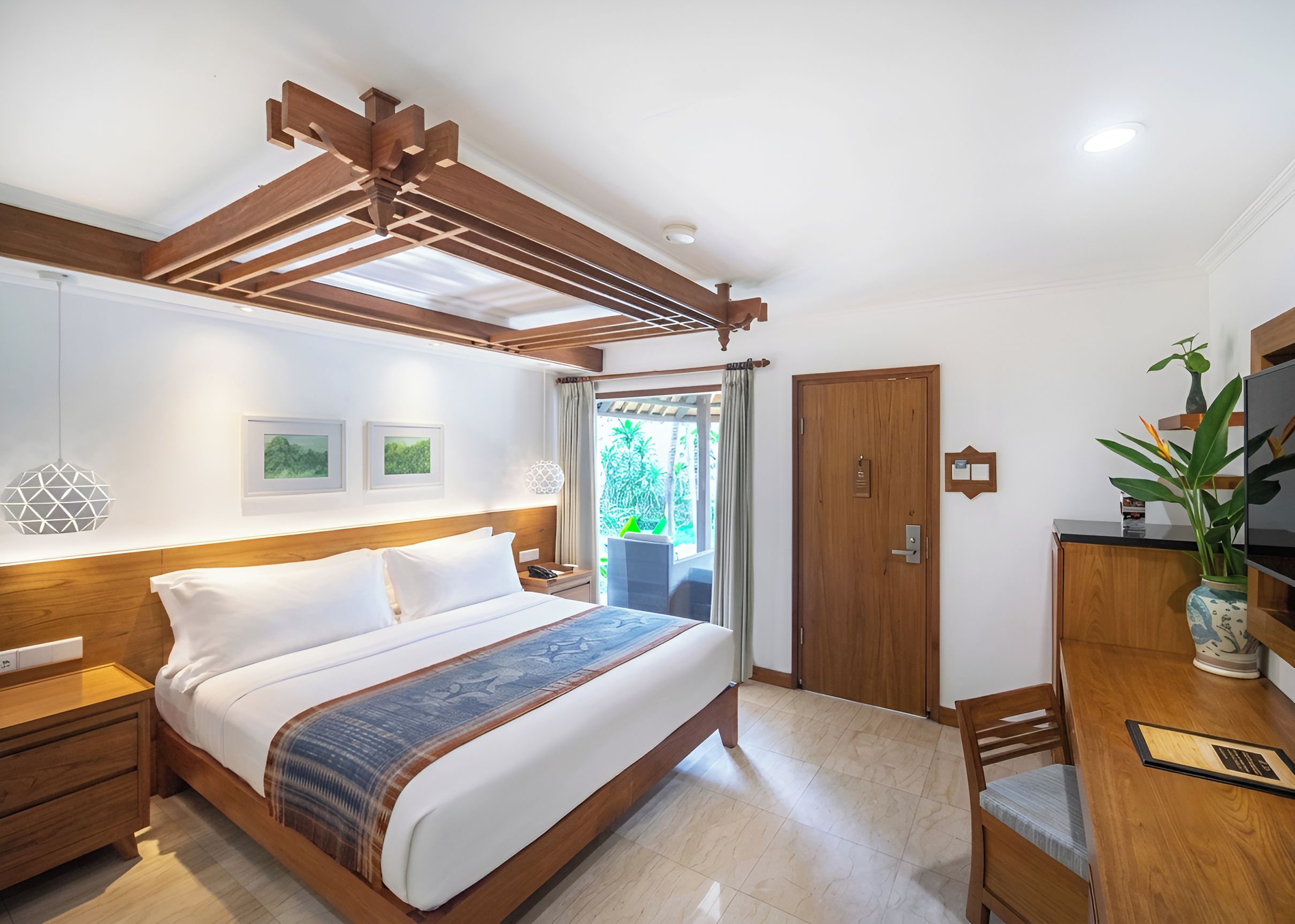 A hotel room with a wooden bed, a desk with a chair, a door, and a window with curtains.