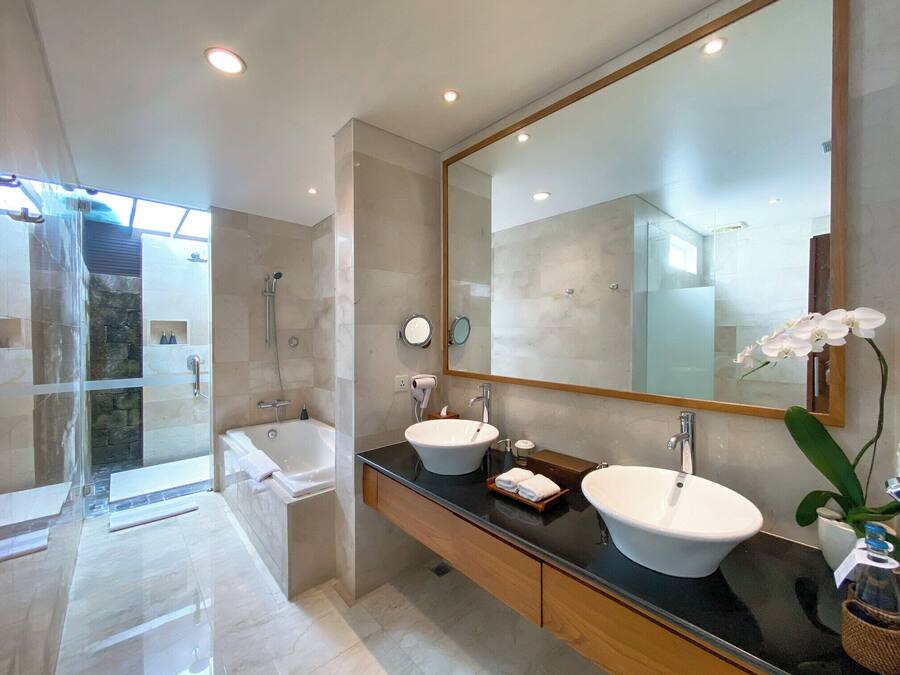 A modern bathroom with a glass shower enclosure, a bathtub, two sinks, and a large mirror.