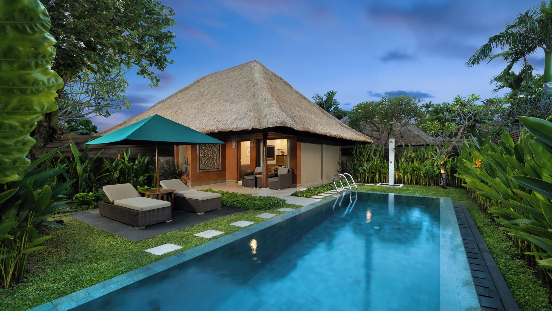 A poolside area with a thatched-roof structure, lounge chairs, and a clear blue pool.
