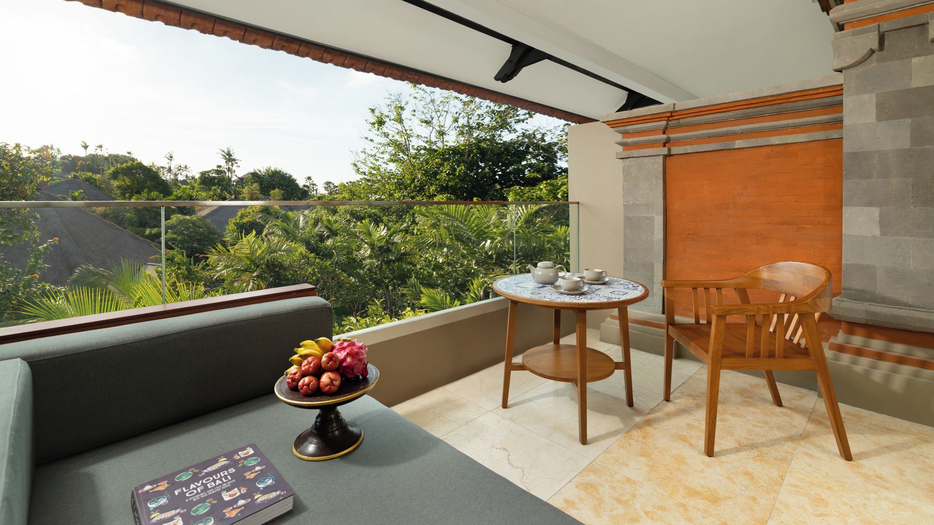 A balcony with a sofa, a table with a teapot and cups, and a fruit bowl.