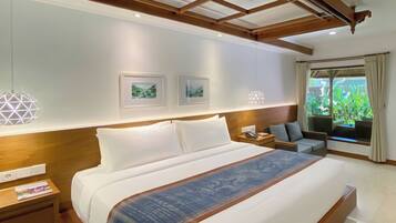 A hotel room with a large bed, two bedside tables, a nightstand, a sofa, a window with curtains, and two framed pictures on the wall.