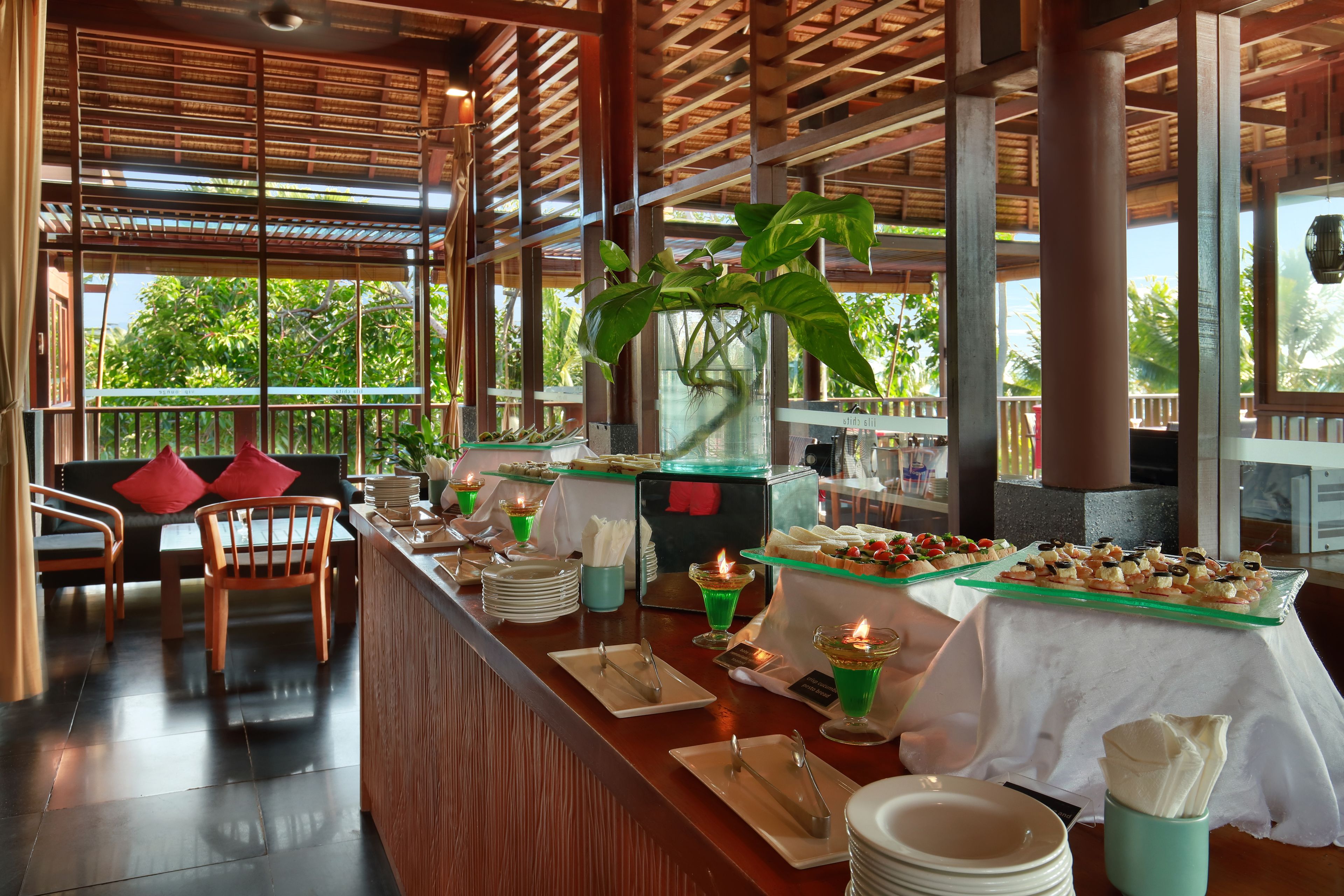 Montaje tipo buffet con diversos alimentos, un área de comedor con sillas y un amplio ventanal con vistas a zonas verdes.