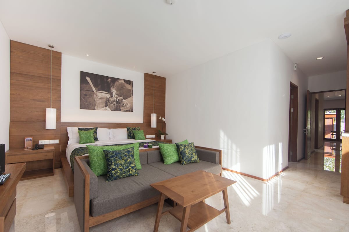 A modern hotel room with a large bed, a sofa, a wooden coffee table, and a painting on the wall.
