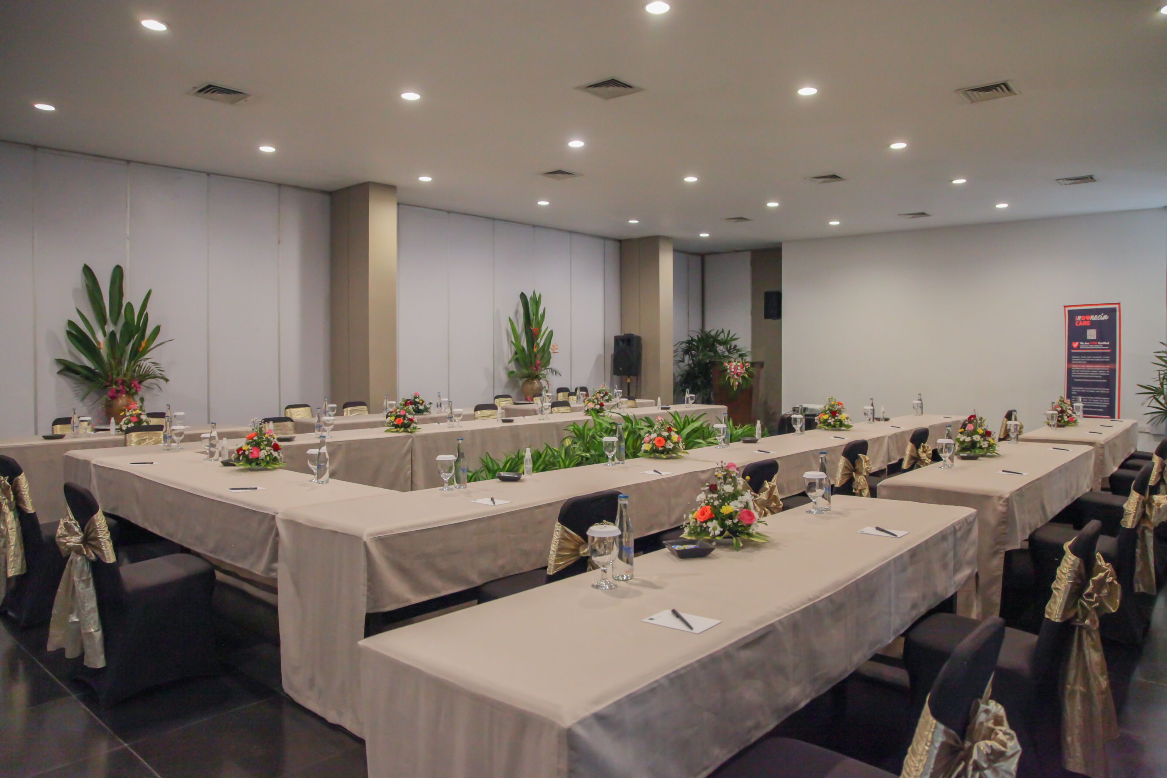 Ein Konferenzraum mit langen Tischen, Stühlen und floralen Tischdekorationen.