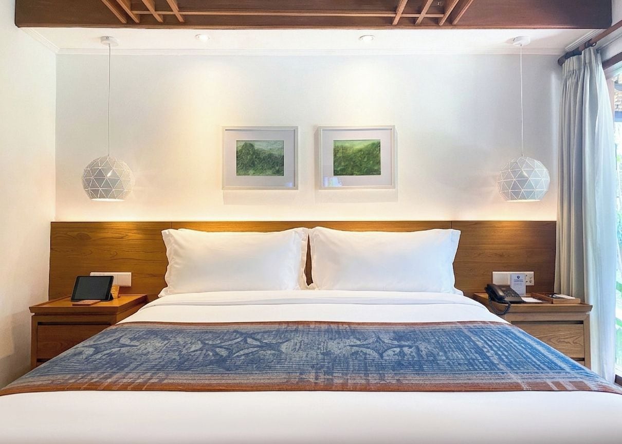 A hotel room with a large bed, two bedside tables, a wooden headboard, and two framed pictures on the wall.