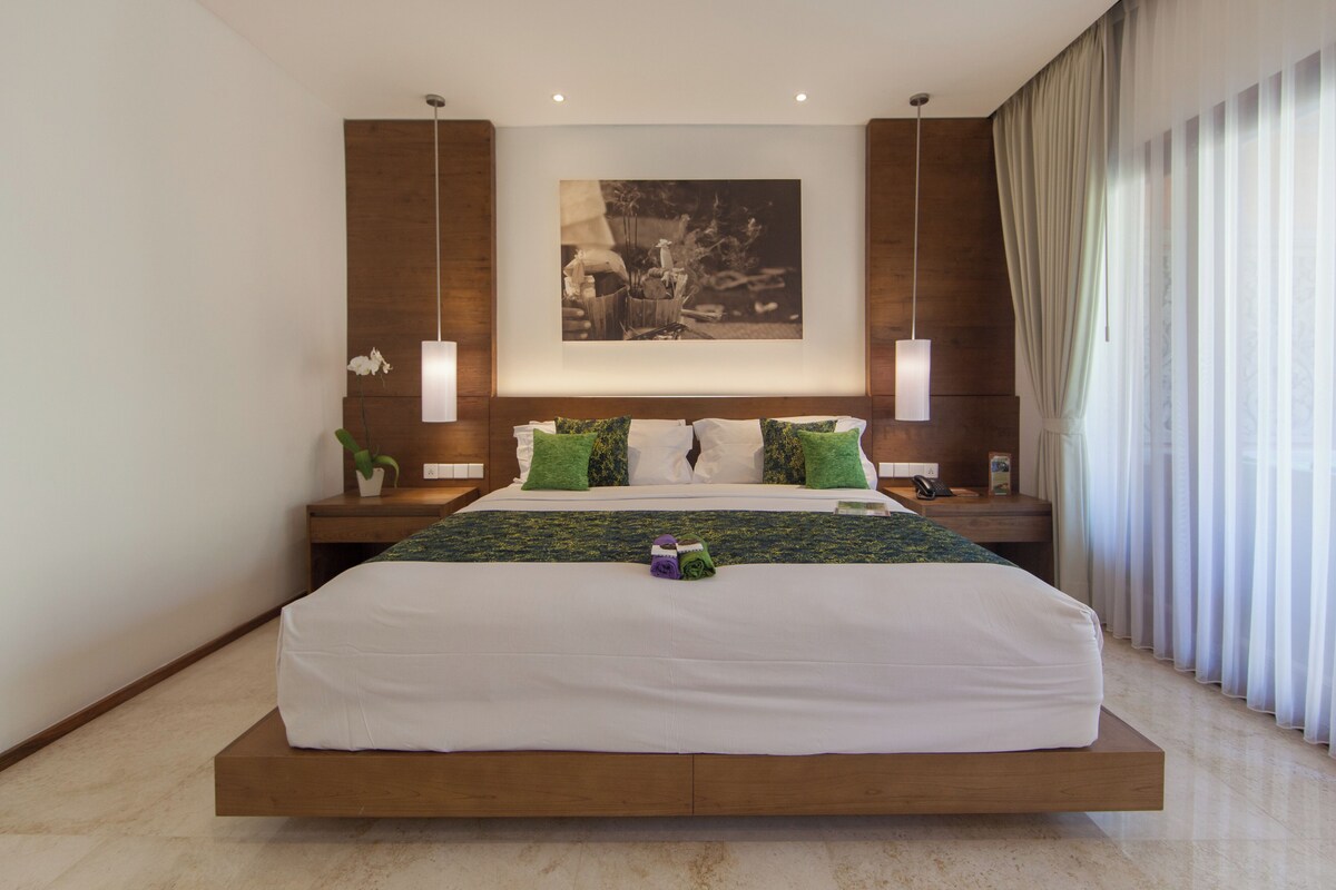 Una habitación de hotel moderna con una cama grande, cabecera de madera y un cuadro sobre la cama.